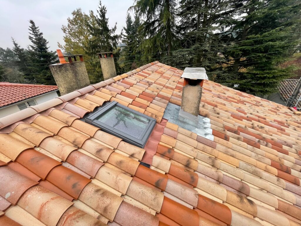 Toiture en tuiles : pose de fenêtre de toit et cheminée Toiture en tuiles canal avec fenêtre de toit Velux et conduit de cheminée sous un ciel nuageux.