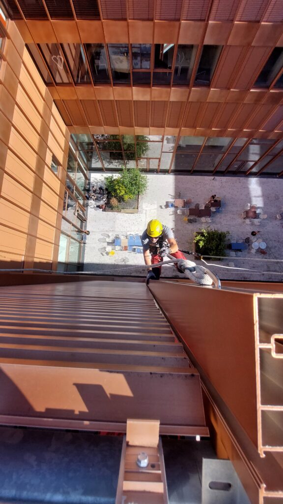 Expert cordiste : Travail en rappel sur façade moderne Cordiste en rappel descendant une façade cuivrée moderne.