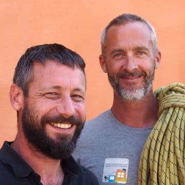 Cordistes Acroclos : professionnels de travaux en hauteur Deux grimpeurs barbus souriants avec corde jaune devant un mur orange. Logo ACROCLOS sur le t-shirt.