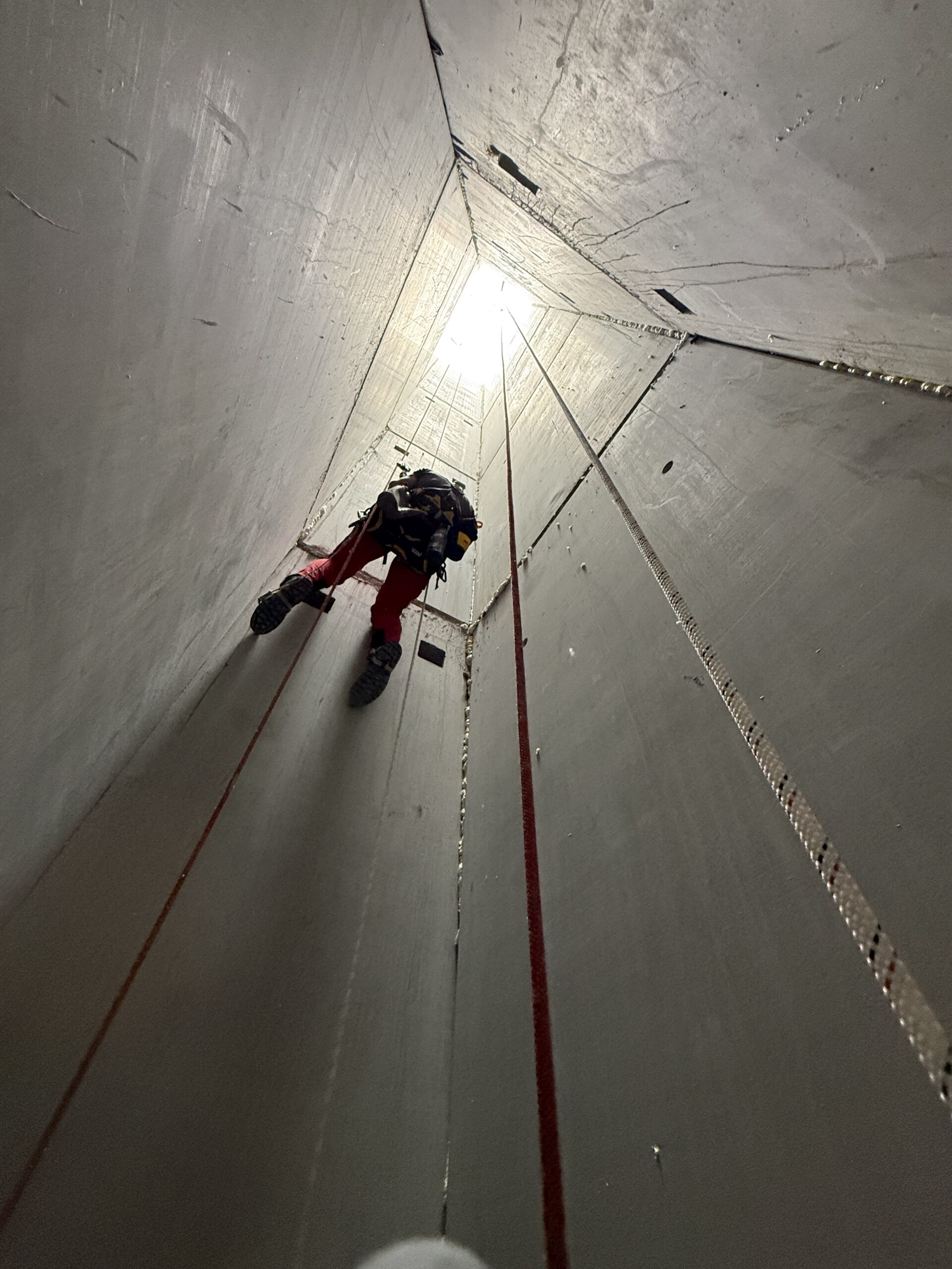 Descente en rappel dans un puits étroit en béton Technicien cordiste descendant en rappel dans un puits industriel en béton étroit.
